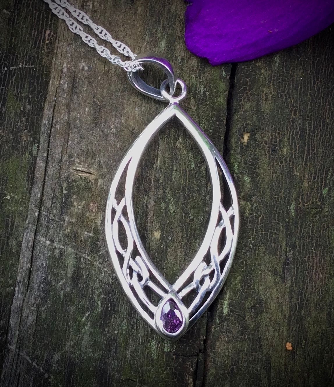 Sterling silver oval Celtic knot pendant on bark with an  amethyst-colored gemstone.
