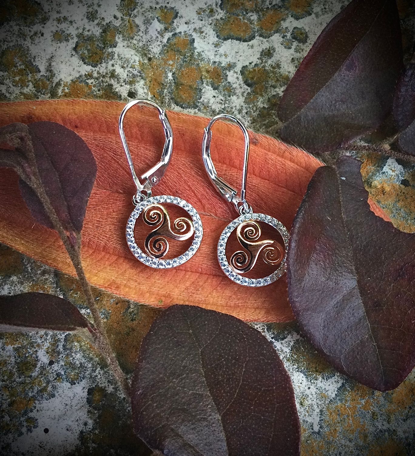 Rose Gold Plated Sterling Silver Triskele Earrings with CZ Stones Sterling silver gold-plated Celtic triskele earrings, handcrafted Irish jewelry, on orange leaf.