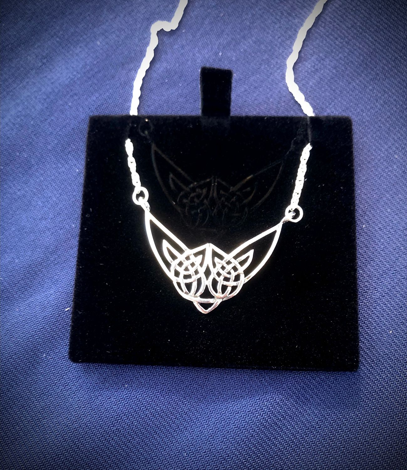 Sterling silver Highland Cow necklet, celebrating Scottish heritage and Celtic design, shown on black jewelry holder. 