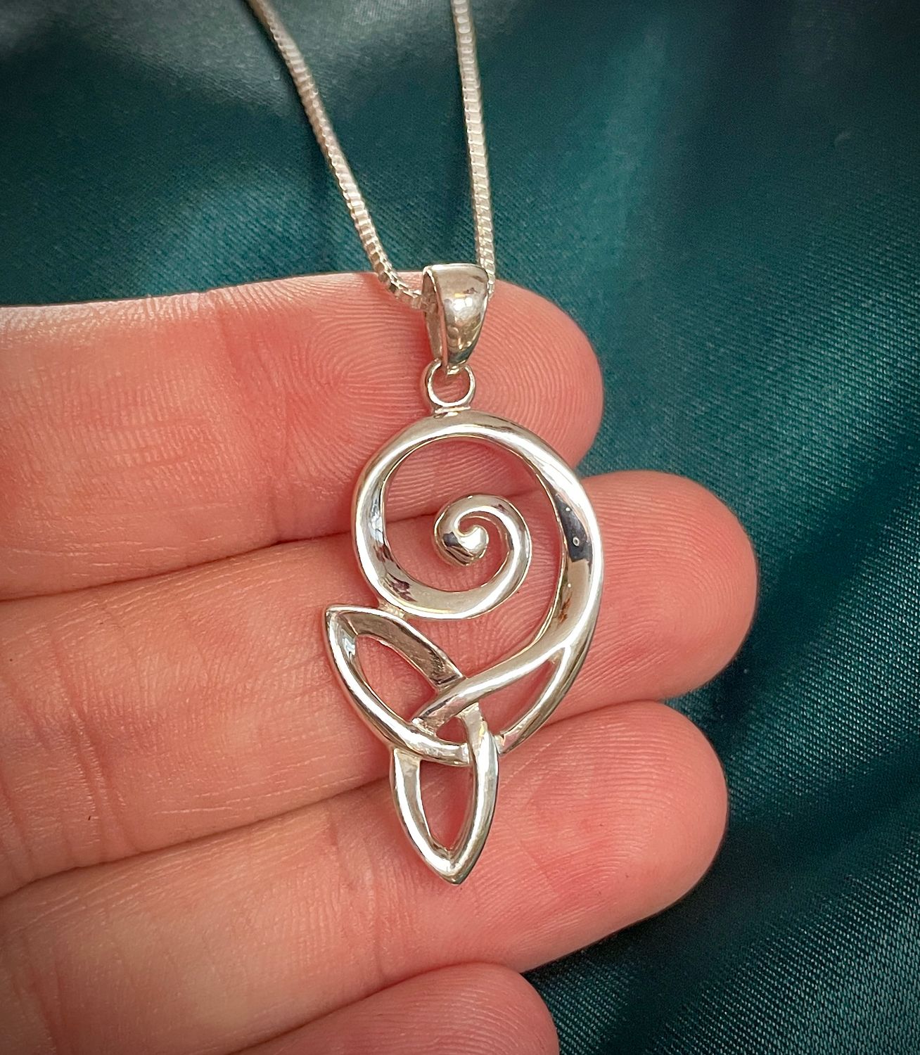 Sterling silver Trinity Knot necklace with swirl, Celtic-inspired jewelry for women’s gifting, held in model's hand. 