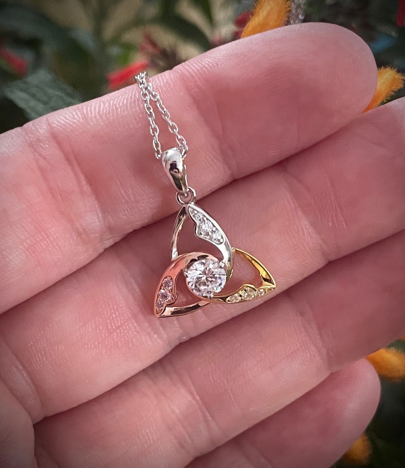 Tri-color Trinity Knot Celtic pendant in sterling silver with rose and yellow gold plating and central CZ stone, on hand. 