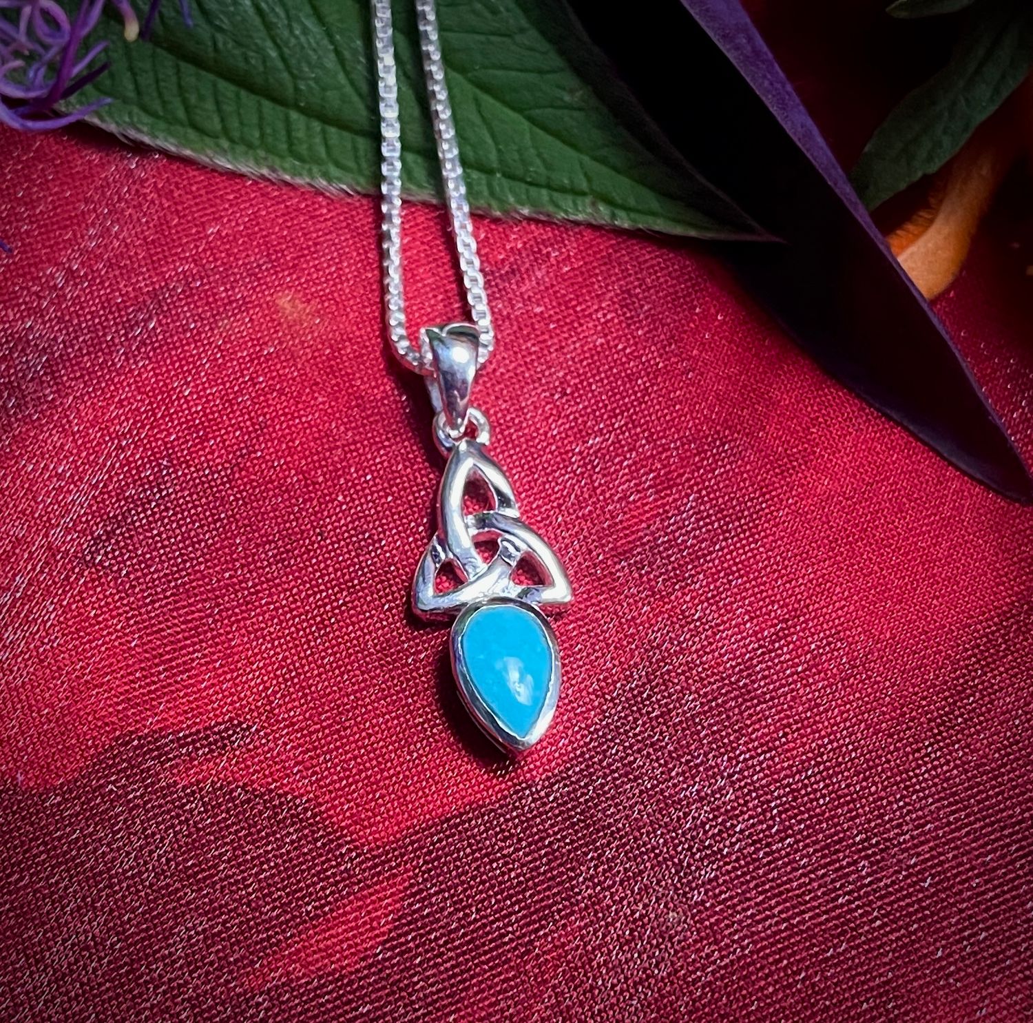 Handcrafted Celtic Trinity Knot pendant on red fabric with aquamarine stone.