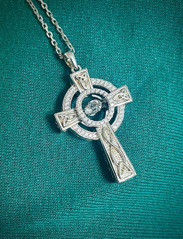 Sterling Silver Celtic Cross with Celtic Knotwork and a central cubic zirconium dancing gemstone, on fabric. 